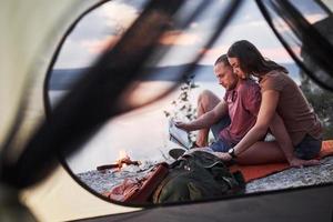 Blick vom Zelt eines Paares mit einer Karte, die während der Wanderung einen Blick auf den See hat. Avel Lifestyle Konzept Abenteuerurlaub im Freien foto