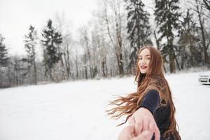 Beeil dich bitte. Mädchen mit langen Haaren geht im Winter in der Nähe des Waldes zum Auto foto