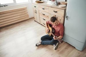 Routine üben. musiker spielt an seinem wochenende zu hause in der küche auf der akustikgitarre foto