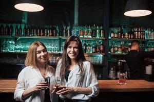 Zwei Freundinnen haben eine schöne Zeit im Nachtclub in der Nähe der Bar des Nachtclubs und lächeln foto