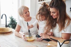 dass das Mischen fast fertig ist. Mutter, Großmutter und Tochter amüsieren sich in der Küche foto