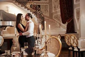 Typ wird seine Frau küssen. Schönes Paar hat abends ein romantisches Abendessen im Luxusrestaurant foto