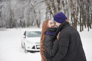 ineinander verliebt. Wunderschönes junges Paar steht vor ihrem weißen Auto im verschneiten Wald foto