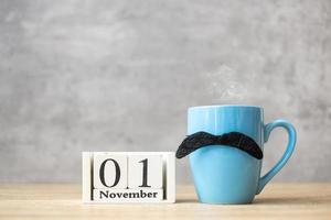 1. november kalender, blaue kaffeetasse oder teebecher und schwarzer schnurrbartdekor auf dem tisch. männertag, glücklicher vatertag und hallo november-konzept foto