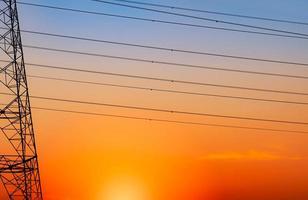 Silhouette Hochspannungsmast und Elektrokabel mit einem orangefarbenen Himmel. Strommasten bei Sonnenuntergang. Kraft- und Energiekonzept. Hochspannungsnetzturm mit Drahtkabel an der Verteilerstation. foto