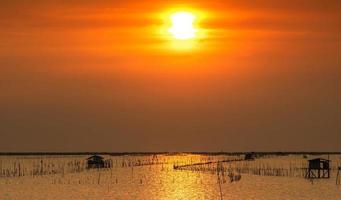 schöne sonne im sommer. Sonnenuntergangshimmel über dem Meer, Fischerhütte und Mangrovenwald am Abend. Bambusstange an der Küste. Bambusstickerei, um die Welle zu verlangsamen und die Küstenerosion zu verhindern. foto