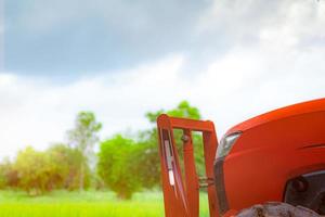 Orangefarbener Traktor, der am grünen Reisfeld geparkt ist. Landmaschinen im landwirtschaftlichen Betrieb. Reisplantage. Reisfarm in Asien. Reisanbau Landwirtschaft. Beschaffenheit des Ackerlandes. Smart-Farming-Konzept. foto