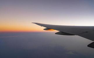 Flügel des Flugzeugs über der Stadt. Flugzeug fliegt am blauen Himmel. malerische Aussicht aus dem Flugzeugfenster. Flug der kommerziellen Fluggesellschaft morgens mit Sonnenlicht. Flugzeugflügel über Wolken. Konzept der Flugmechanik. foto