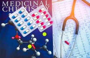 pillen auf lehrbuch der medizinischen chemie und stethoskop auf ekg- oder ekg-elektrokardiogramm-berichtspapier. Konzept zur Erforschung der Wirkstoffstruktur. kardiologie und antibiotikaresistenzkonzept. foto