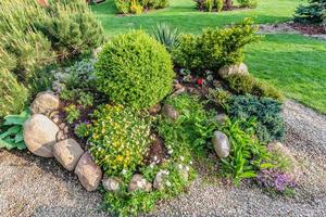 landschaftlich gestalteter Sommergarten mit grünen Pflanzen, Felsen, Blumen in Blumenbeeten, gemähtem Gras. foto