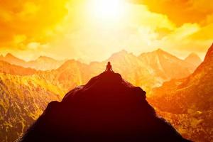 Frau meditiert in sitzender Yoga-Position auf der Spitze eines Berges über Wolken bei Sonnenuntergang. foto