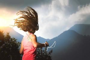 Kleines Mädchen mit ihren Haaren im Wind hört Musik mit Player und Kopfhörern foto