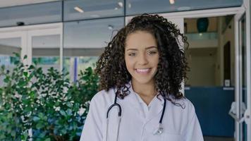 Lateinische junge Ärztin trägt weiße Uniform, weißen Arztkittel, Stethoskop und blickt in die Kamera foto