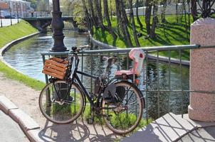 Das Fahrrad ist am Zaun am Flussufer festgeschnallt. Fahrrad mit Kindersitz und Schublade foto