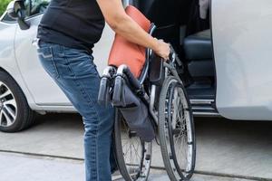 asiatische Frau, die den Rollstuhl in ihr Auto faltet und anhebt. Konzept der Barrierefreiheit. foto