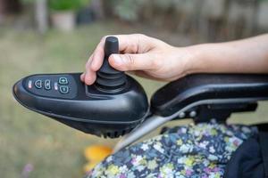 asiatische Patientin auf elektrischem Rollstuhl mit Joystick und Fernbedienung auf der Krankenstation, gesundes, starkes medizinisches Konzept foto