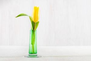 Einzelne frische Tulpe in einer Glasvase auf einem Holztisch. foto