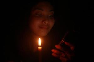 asiatische frau, die zu ihrem handy mit kerze in der dunklen nacht lächelt foto