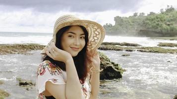 Ein junges asiatisches Mädchen mit Strandhut entspannt sich am Strand mit blauem Himmel in Gunungkidul, Indonesien foto