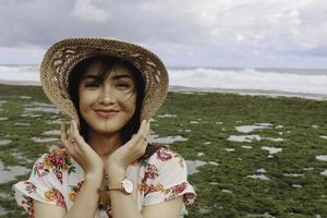 Ein junges asiatisches Mädchen mit Strandhut entspannt sich am Strand mit blauem Himmel in Gunungkidul, Indonesien foto