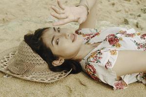 Eine junge schöne asiatische Frau, die vom Licht geblendet wird, während sie auf dem Strandsand liegt foto