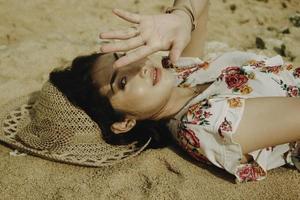 Eine junge schöne asiatische Frau, die vom Licht geblendet wird, während sie auf dem Strandsand liegt foto