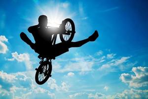 Mann springt auf BMX-Rad und führt einen Trick gegen den sonnigen Himmel aus foto