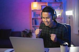 asiatischer einflussmann lächelt youtuber live-streaming oder arbeitskonferenz mit laptop und kopfhörer tragen. asiatischer mann, der online unterrichtet. foto