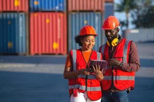 Fröhliche afroamerikanische Arbeiterinnen und Arbeiter, die während eines Videoanrufs in einem Logistikcontainer-Hof ein Tablet verwenden. foto