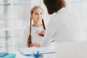 hausarzt der familie untersucht kind, hört lungen mit stethoskop ab, stellt verschreibungspflichtige pose in moren krankenhausbüro. krankes Kind ist erkältet, kommt zum Kinderarzt, um sich gut beraten zu lassen, hat Gesundheitscheck foto