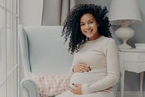 schöne schwangere afrikanische frau, die die schwangerschaft genießt und zeit zu hause verbringt foto