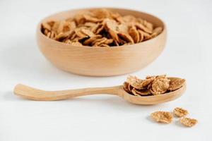 Knusprige, gesunde, trockene Getreideflocken in einer Holzschale mit Holzlöffel auf weißem Hintergrund foto