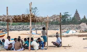 mamallapuram, tamil nadu, indien - august 2018 eine große gruppe indischer fischer, die zusammen unter einem strohzelt am strand in der stadt mahabalipuram sitzen. foto