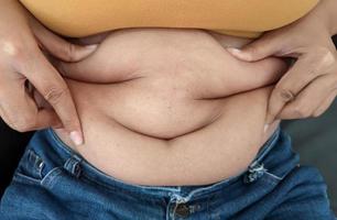 asiatische frauen sitzen auf zeigen körperfett bauch von gerne essen. foto