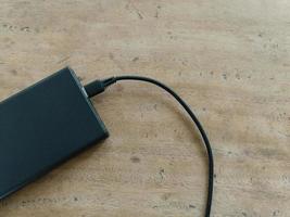 Schwarze Powerbank mit USB-Kabel auf braunem Holzhintergrund. foto