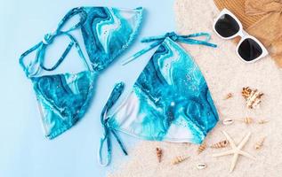 Draufsicht auf Bikini und Sonnenbrille, Sandalen mit Strandzubehör auf blauem Hintergrund. Sommerzeit-Konzept. foto