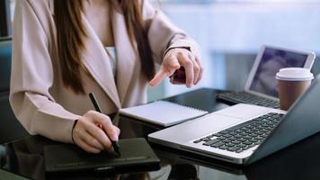 Selbstbewusste Geschäftsfrau, die an ihrem Arbeitsplatz im Büro an Laptop und Tablet arbeitet. foto