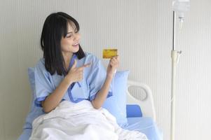 eine junge geduldige frau hält eine kreditkarte in der hand und lässt im krankenhaus ein gesundheitskonzept ein foto