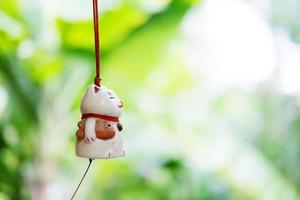 maneki neko ist eine japanische glückliche katzenpuppe, die am fenster mit grünem naturhintergrund hängt foto