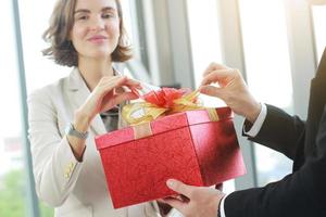 geschäftsmann überraschen und geben rote geschenkbox für geschäftsfrau im büro zum geburtstag. weihnachten, frohes neues jahr und valentinstag konzept. auf rotem Geschenkkarton geschlossen. foto