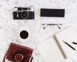 flache Lage, Draufsicht Bürotisch Schreibtisch. schreibtischarbeitsplatz mit retro-kamera, tagebuch, stift, brille, fall, tasse kaffee auf weißem hintergrund. foto