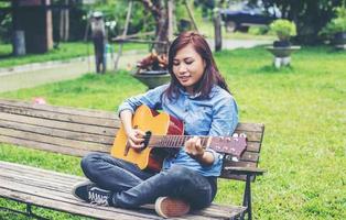 schöne junge frau, die gitarre spielt, sitzt auf einer bank, glückliches zeitkonzept. foto