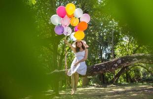 junges jugendlich Mädchen, das auf Baum sitzt und Luftballons in der Hand hält foto