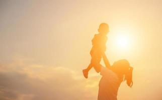 Silhouetten von Mutter und kleiner Tochter, die bei Sonnenuntergang spazieren gehen foto