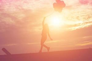 Silhouette einer jungen Frau, die bunte Luftballons mit Sonnenuntergang hält foto