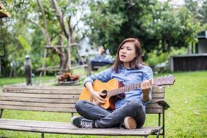 schöne junge frau, die gitarre spielt, sitzt auf einer bank, glückliches zeitkonzept. foto