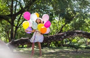 junges jugendlich Mädchen, das auf Baum sitzt und Luftballons in der Hand hält foto