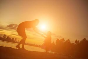 Silhouetten von Mutter und kleiner Tochter, die bei Sonnenuntergang spazieren gehen foto