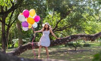 junges jugendlich Mädchen, das auf Baum sitzt und Luftballons in der Hand hält foto