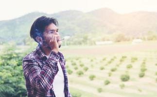 Hipster-Mann raucht Zigarette und steht hinter einem Berg. an der frischen Luft am Morgen. foto